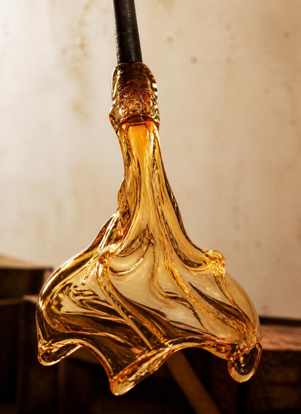 Molten amber glass mid-formation in warm studio light
